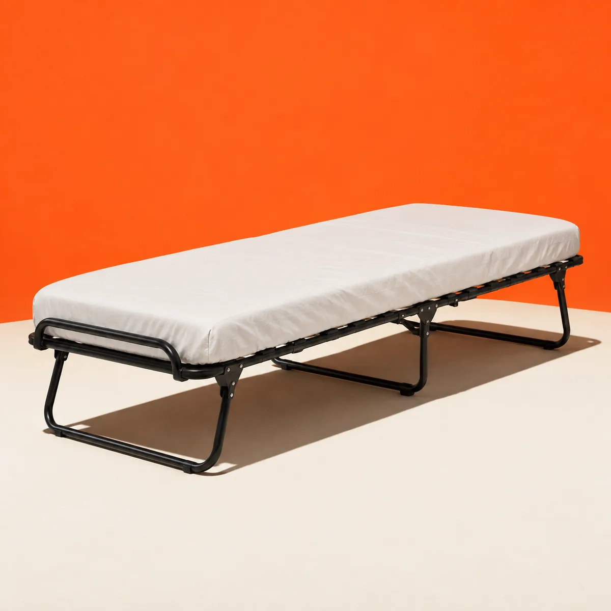 Opklapbaar logeerbed met zwart frame en witte matras tegen oranje wand.