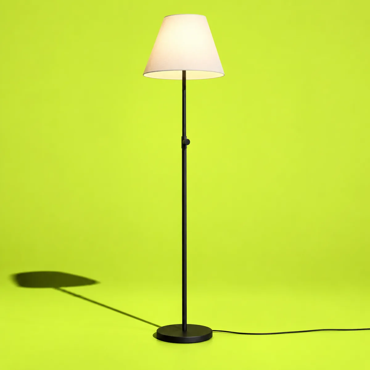 Vloerlamp met zwart frame en crèmekleurige kap op lime achtergrond.
